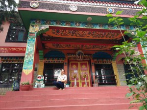 Sitting on the steps to the entrance of the gompa. The pillars and ceiling have paintings of Buddhist themes and sayings
